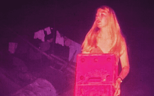 Woman with long hair holding pink box.