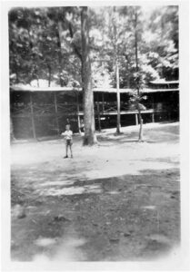 Boy standing near cabin in woods.