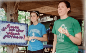 Two girls at summer camp, holding sign.