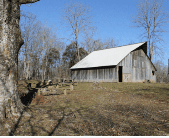 Wooden barn with white roof in a field.