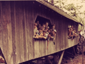 Kids peeking out of a wooden cabin.