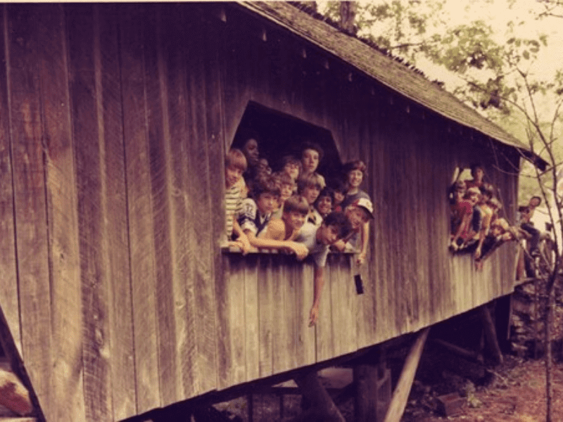 Group of children looking out of wooden structure.