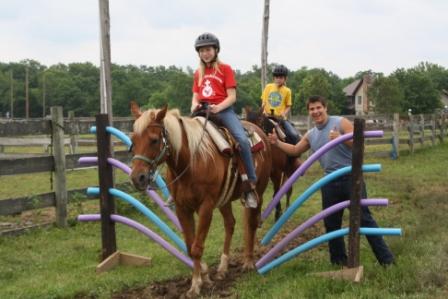 Three people riding horses over poles.