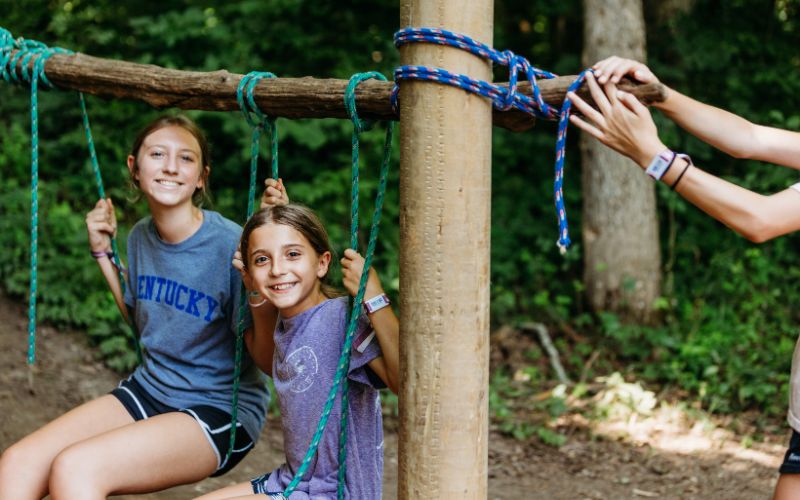 Two girls playing on a rope swing.