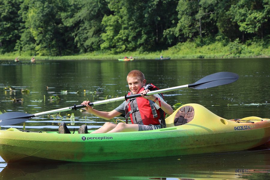 Boy paddling a green kayak on a lake.