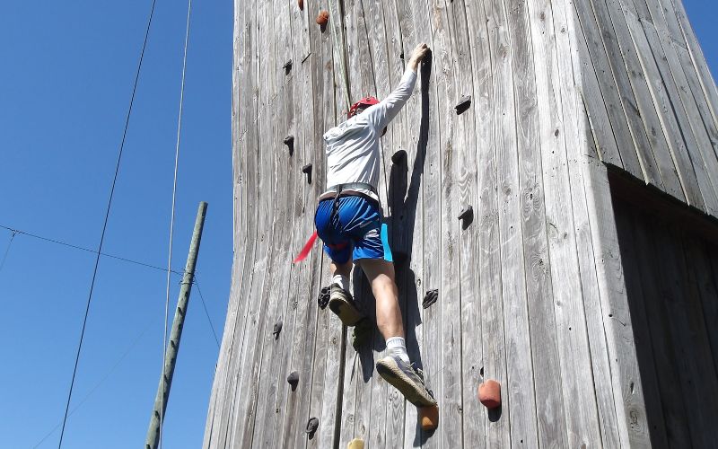 Climber ascending tall wooden outdoor rock wall