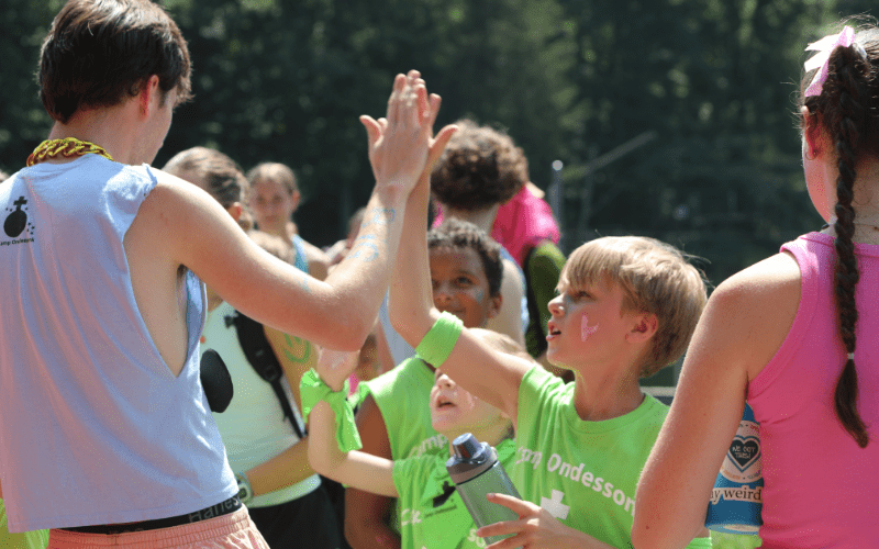 Children high-fiving outdoors at summer camp