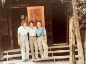 Three women standing outside a cabin.