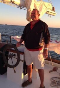 Man on a sailboat with a steering wheel.