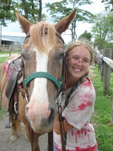 A young woman smiles with a brown horse.