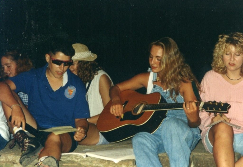 A group of people sitting on a rock, playing an acoustic guitar and creating an echo effect.