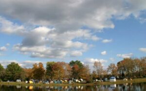 Camping tents by a lake under clouds.