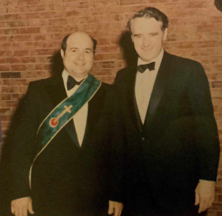 Two men in formal attire, one with a sash.