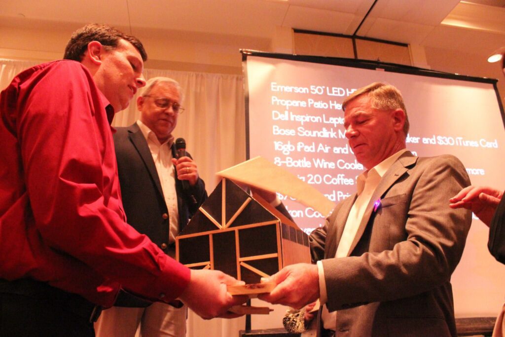 Three men exchanging wooden model at event