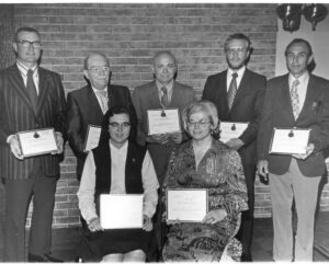 Seven people holding award certificates.