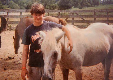 Young boy with his arm around a horse.