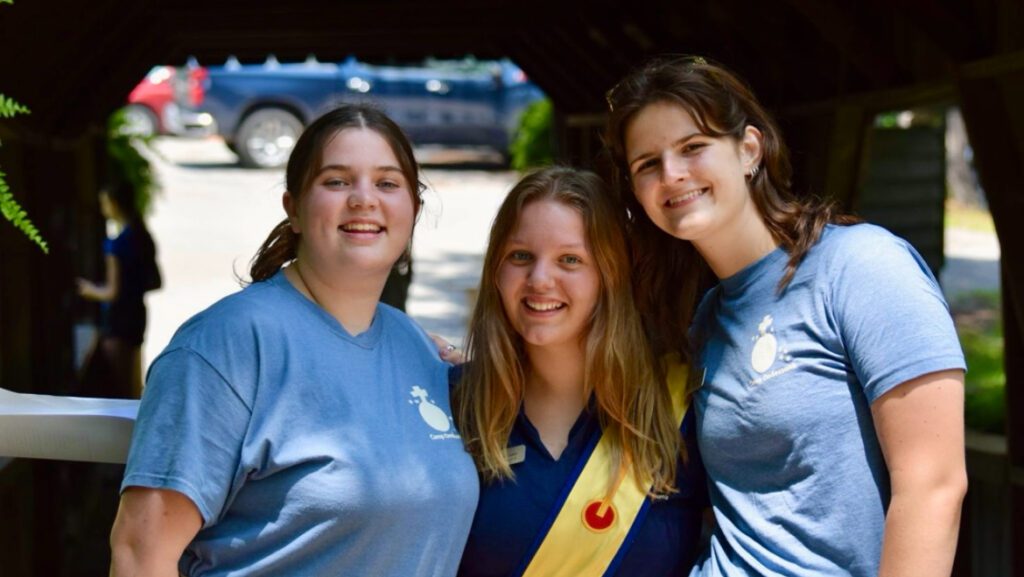 Three smiling teens in blue camp shirts