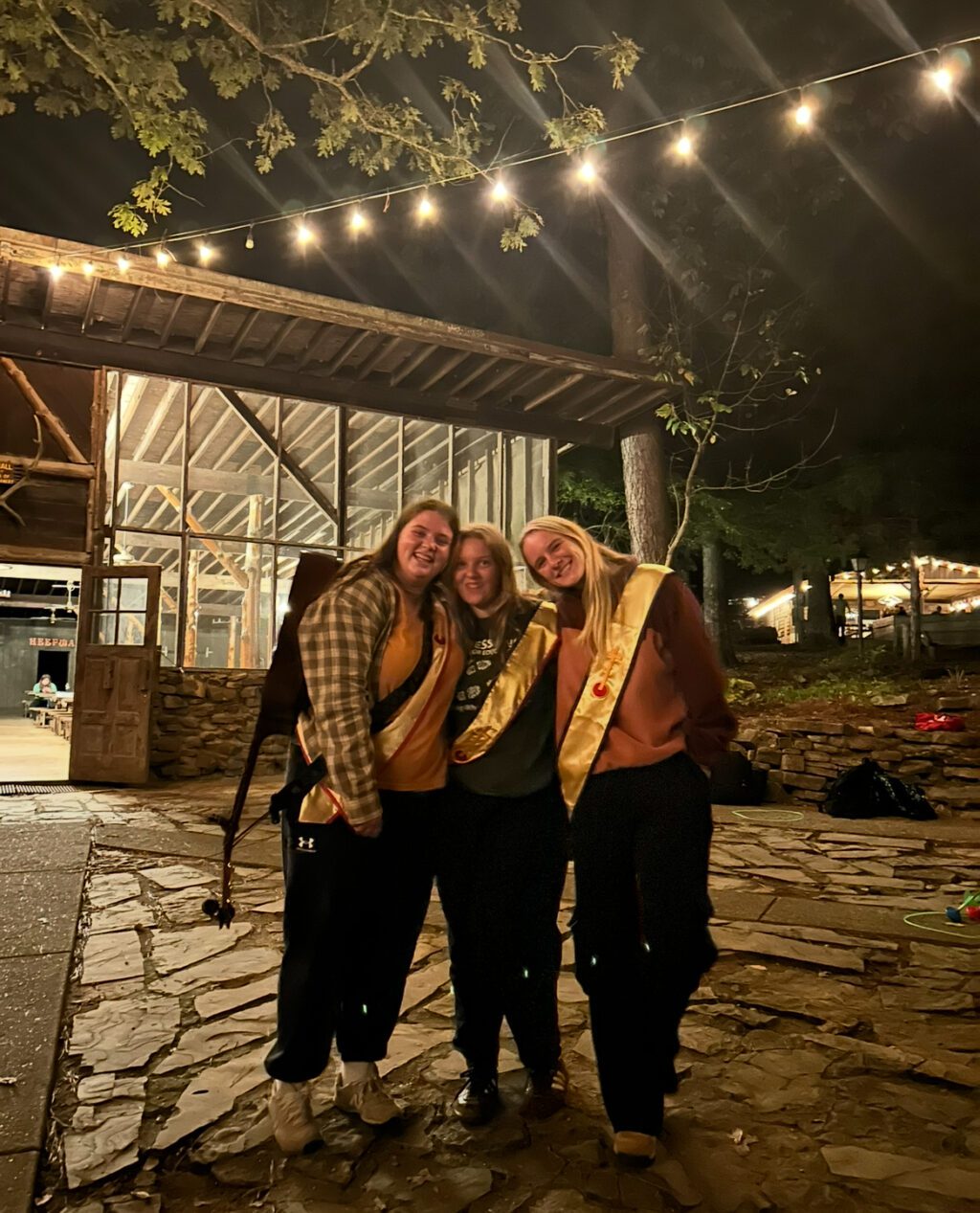 Friends posing with golden sashes under lights