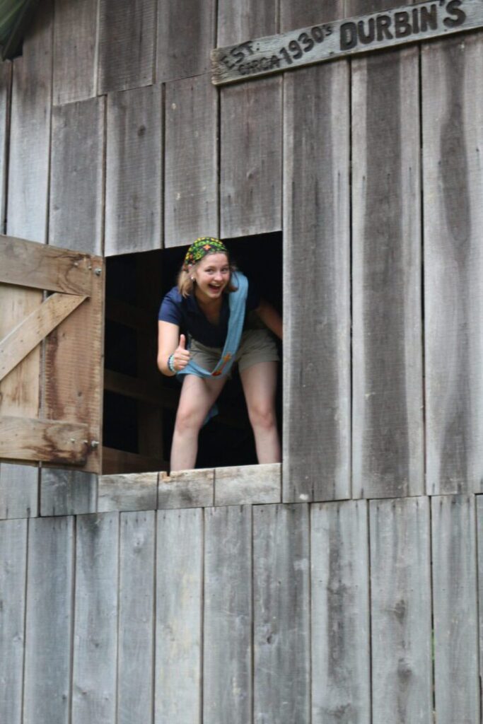 A counselor-in-training reflecting by the window in a barn.