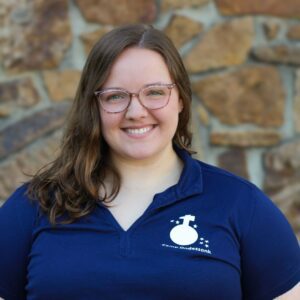 Smiling woman with glasses against stone wall.