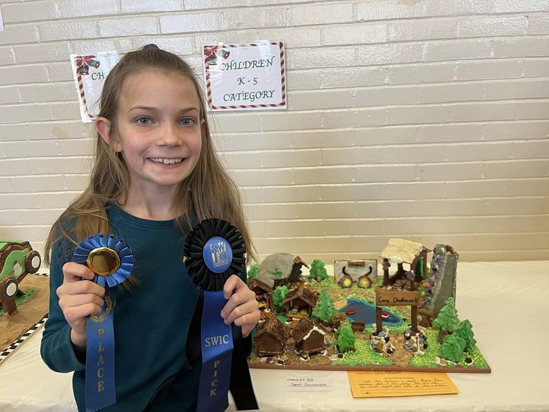 Young girl holding gingerbread house awards.