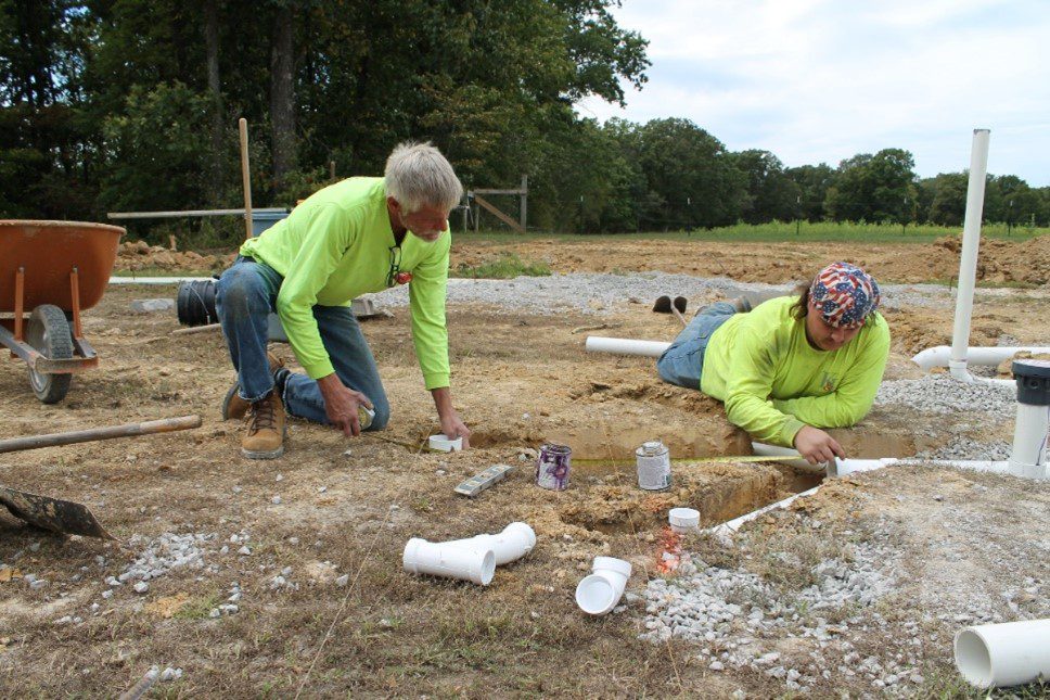 Two men installing PVC pipes in dirt.