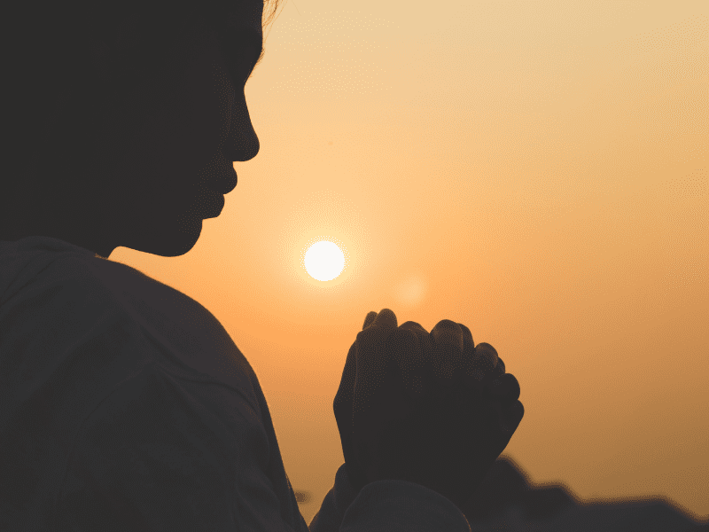 Silhouette of person praying at sunset.