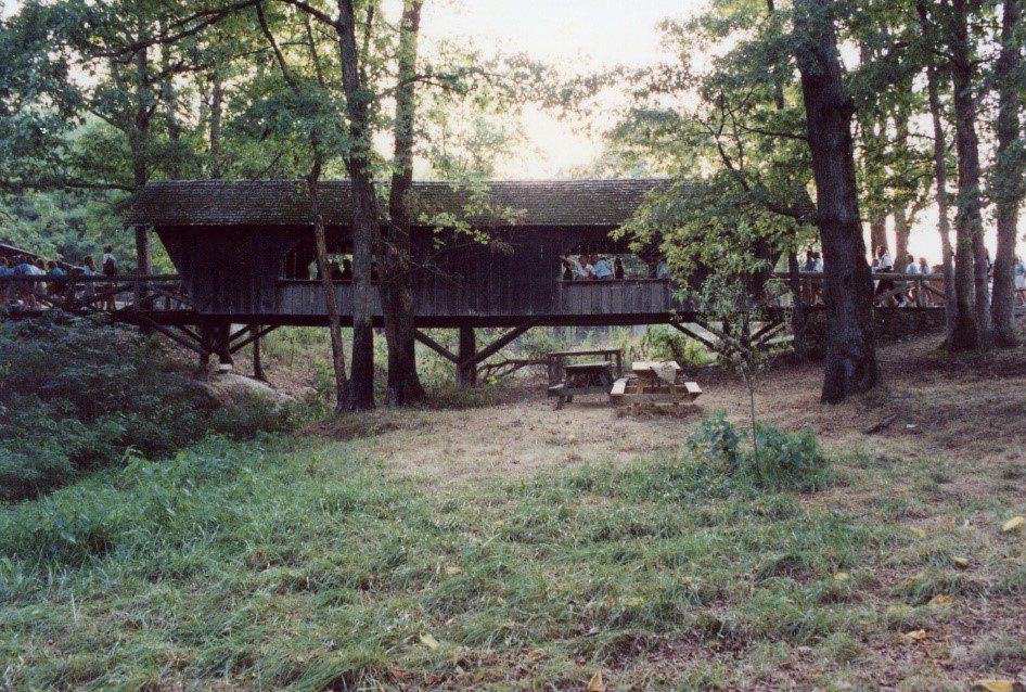 Covered bridge with people and picnic tables.