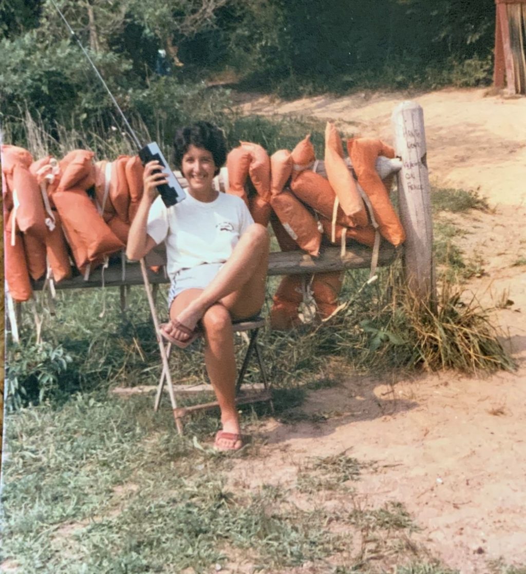Woman sitting by life jackets outdoors.