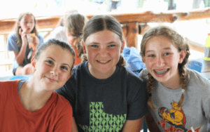 Three girls smiling for a summer camp photo.