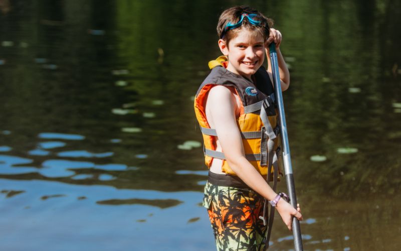 Child smiling while holding a paddle outdoors.