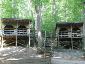 Two wooden cabins on stilts in woods.