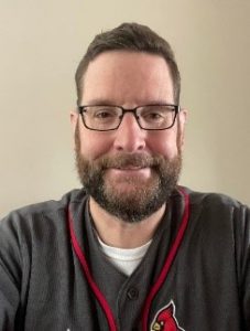 A man with a beard and glasses smiling.
