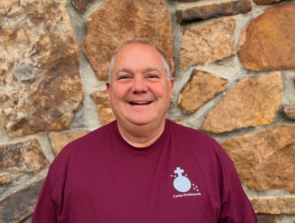 Smiling man in maroon shirt by stone wall