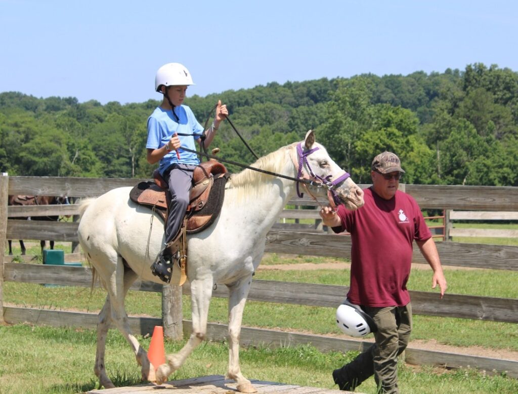 Young rider on white horse with instructor.