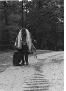 Man with suitcase walks down a road.