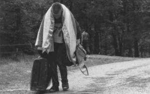 Man carrying suitcase, walking on road.