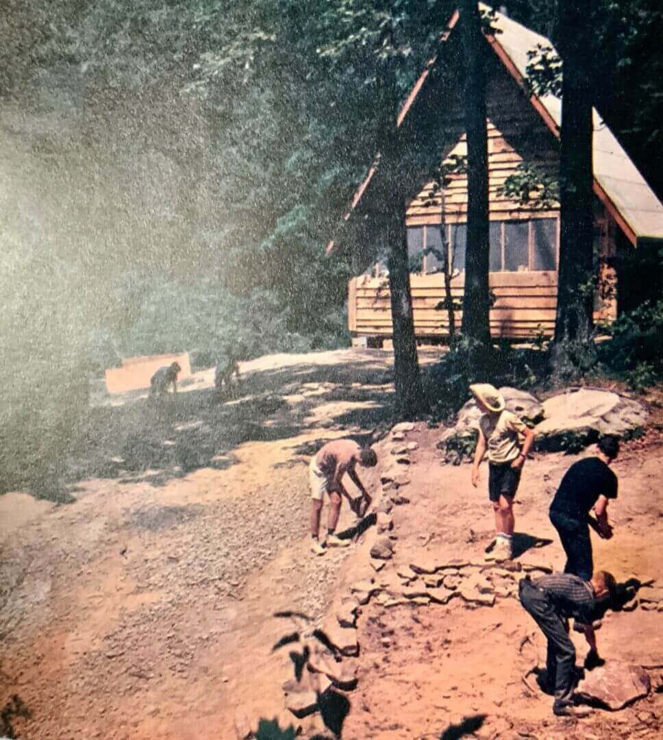 Kids building a stone wall near a cabin.