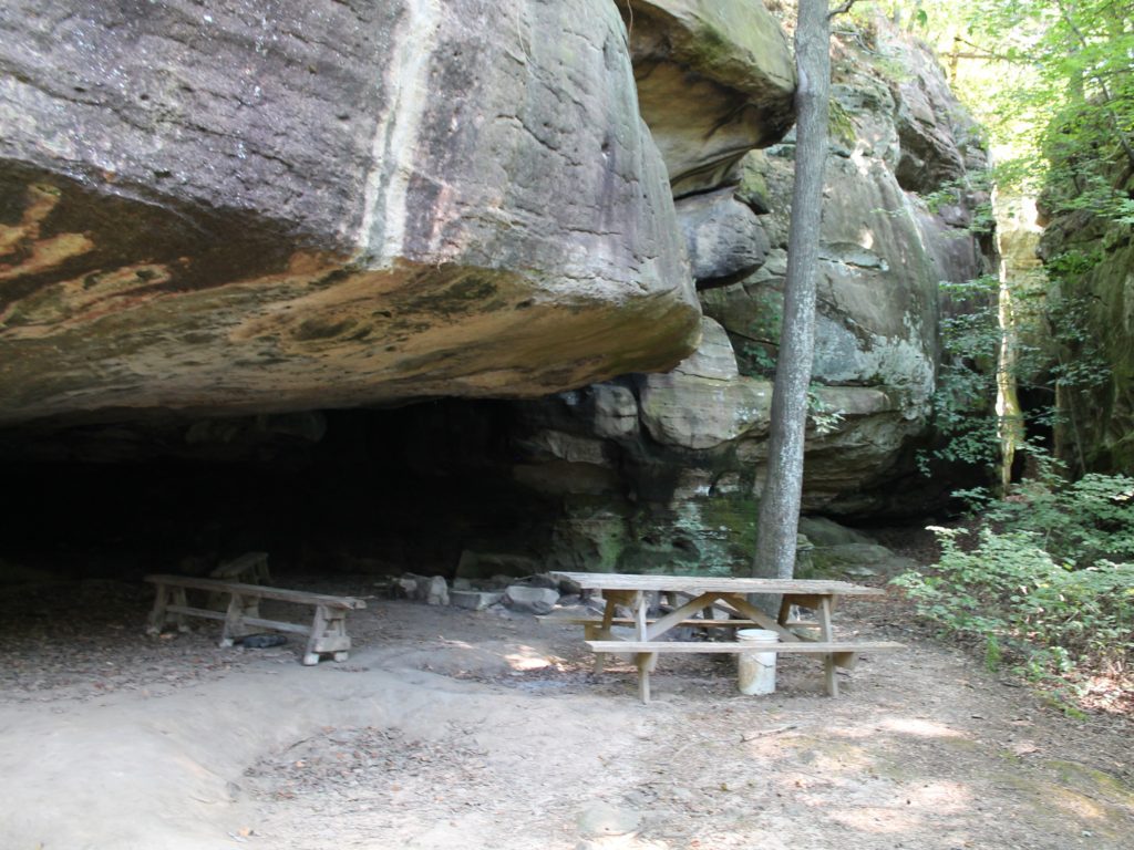 Picnic table and benches under a rock overhang.