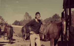 Man with long hair standing next to horse.