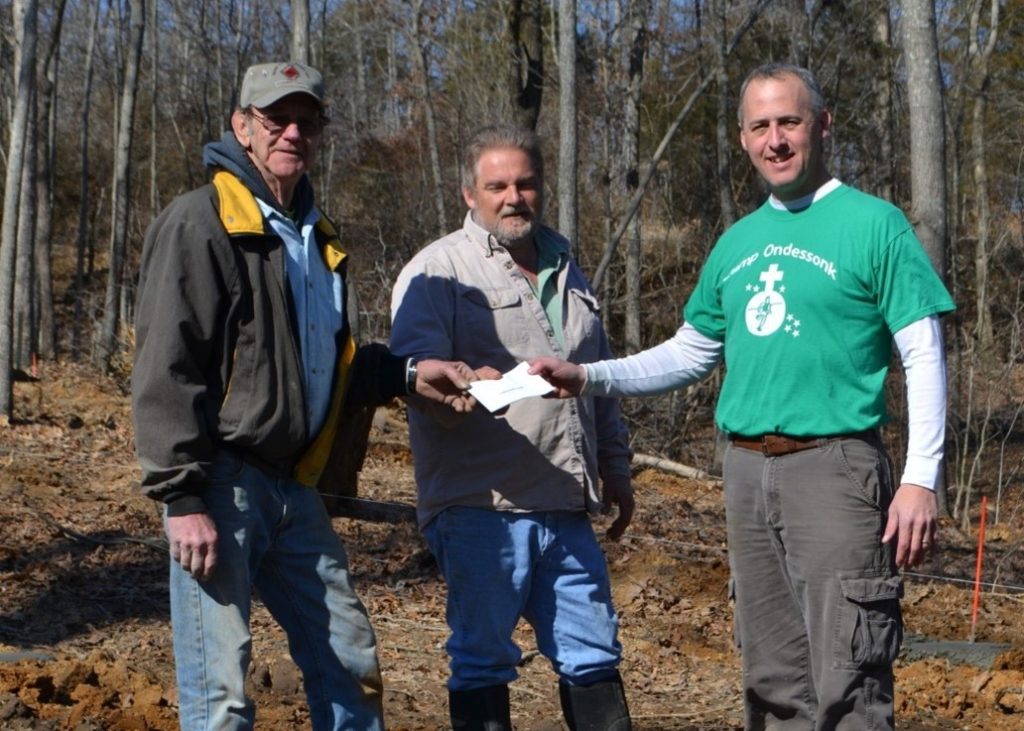 Three men outdoors exchanging a check.
