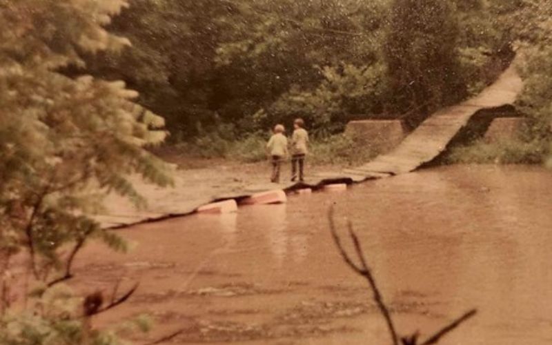 Two people crossing a narrow, rustic bridge.