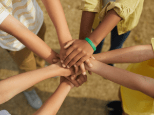 Four kids stacking hands, unity and teamwork.