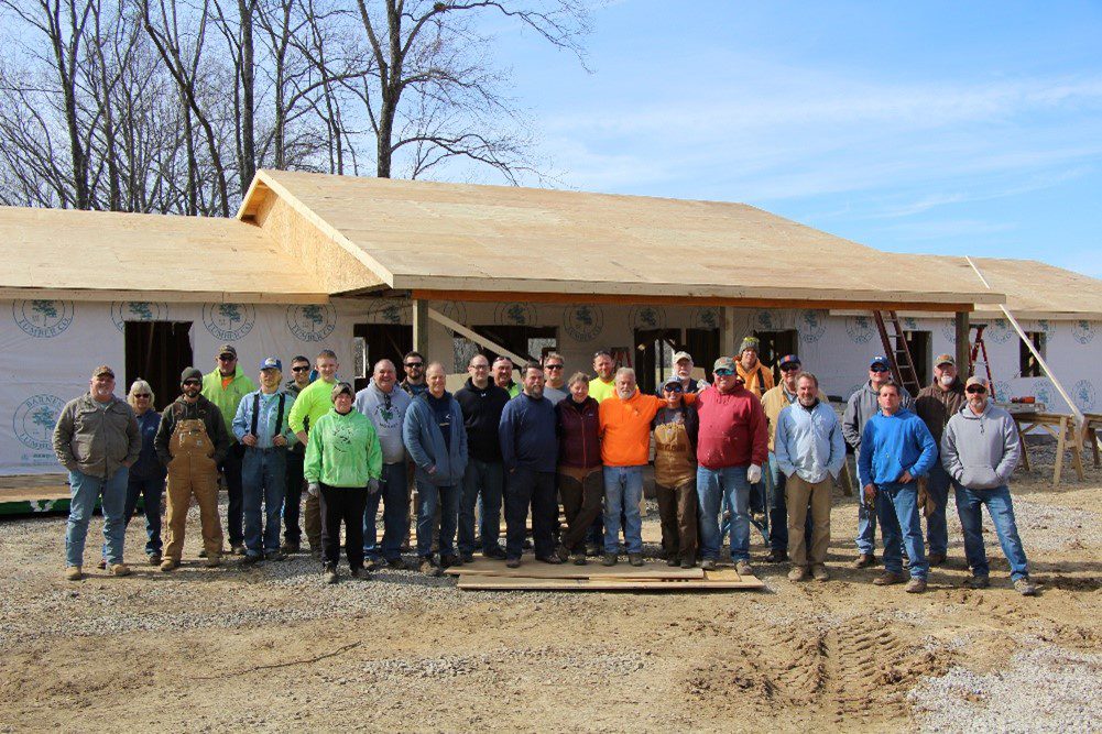 Group of people stand in front of house frame.