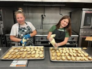 Two girls piping potato skins with filling.