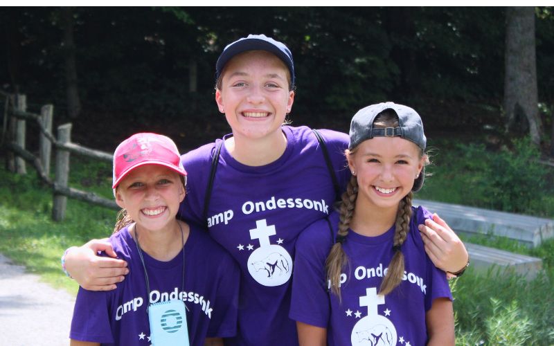 Three smiling girls in purple camp shirts.