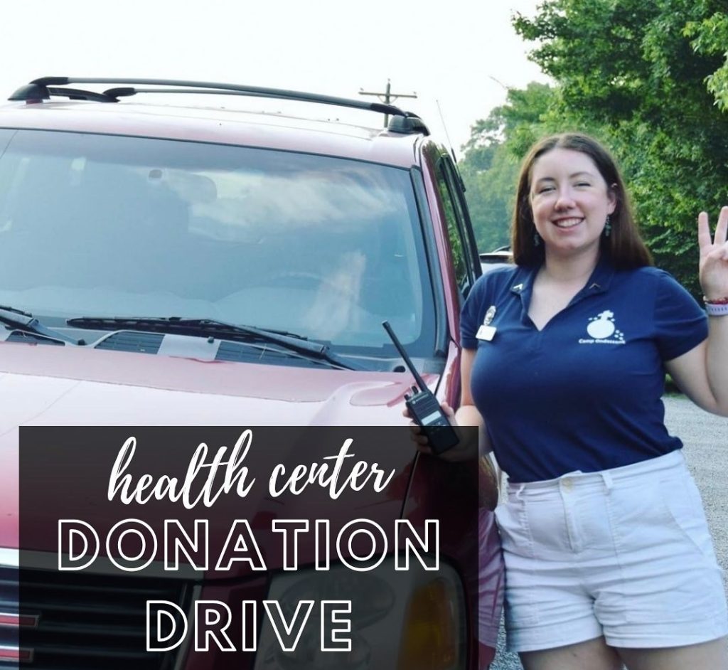 A woman standing next to a Health Center SUV during a donation drive.