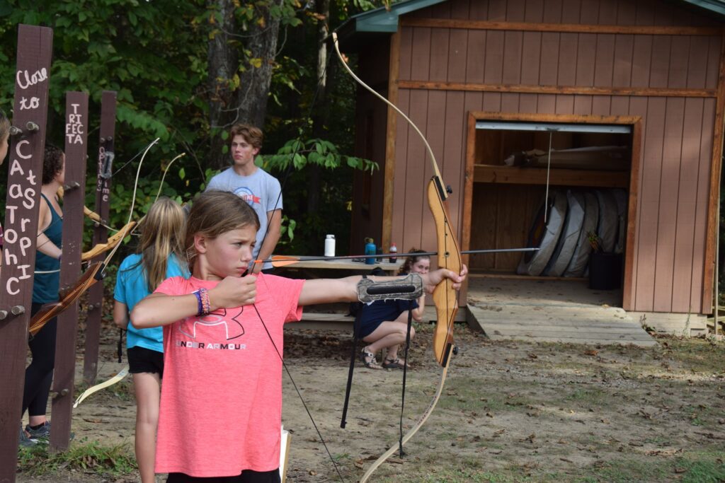 A young girl aiming a bow and arrow with determination and focus, displaying excellent archery skills.