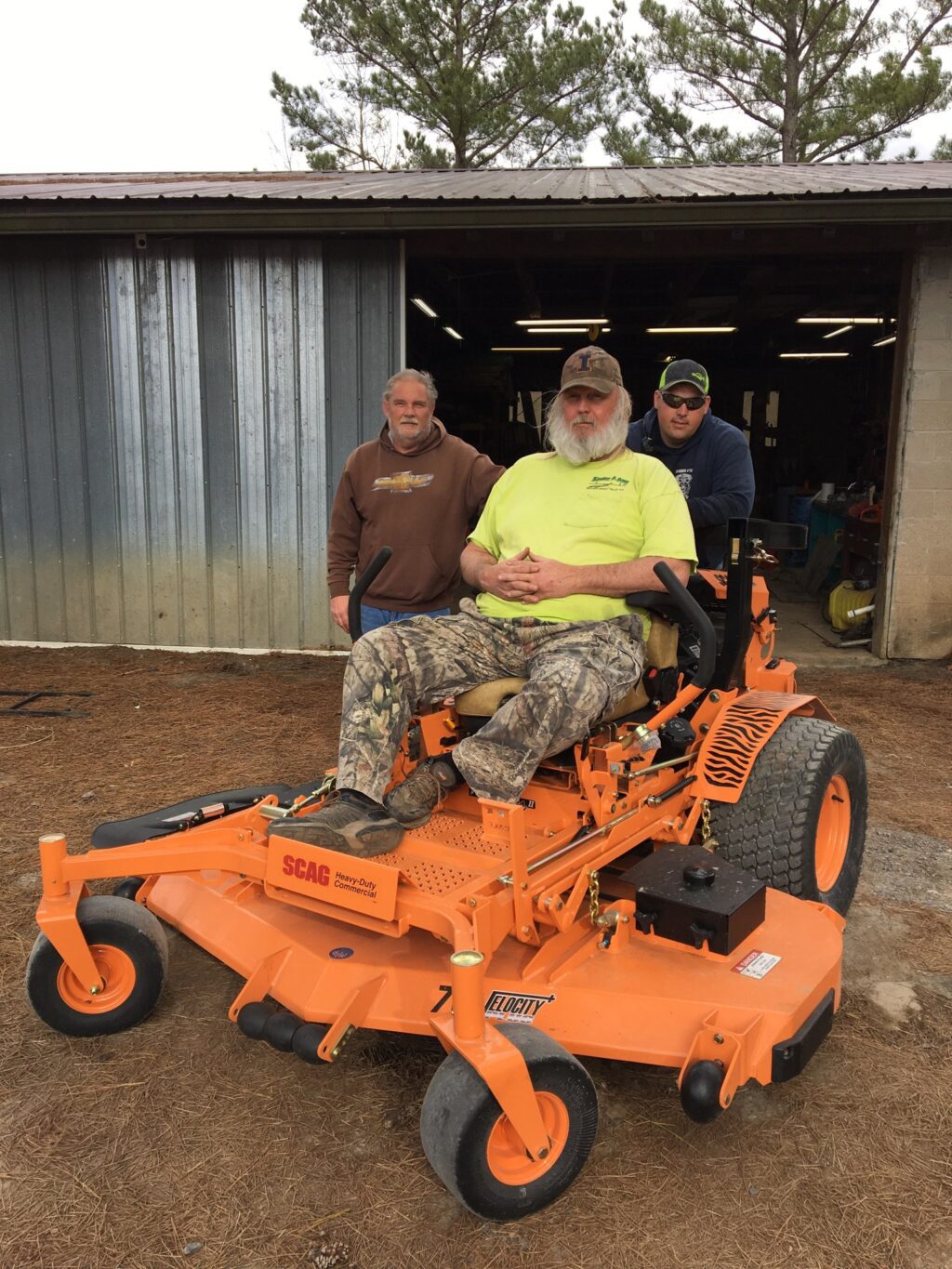 Three men supporting an orange lawn mower.